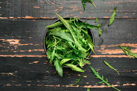 Bowl with fresh arugula on dark wooden background
