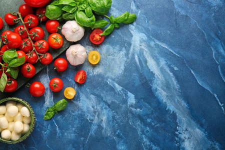 Composition with fresh cherry tomatoes, garlic, basil and mozzarella cheese on color backgroundの写真素材