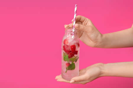 Hands with bottle of fresh strawberry lemonade on color backgroundの写真素材