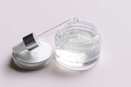 Cosmetic transparent cream jar with pipette on light background