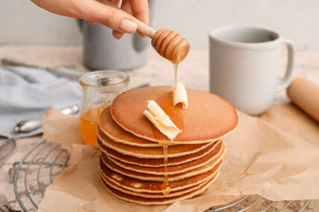 Woman pouring honey onto tasty pancakes