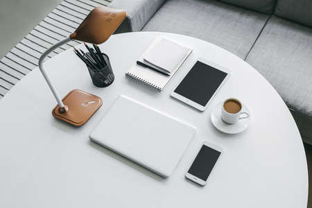 Modern laptop, tablet computer, mobile phone, cup of coffee and stationery on table in roomの写真素材
