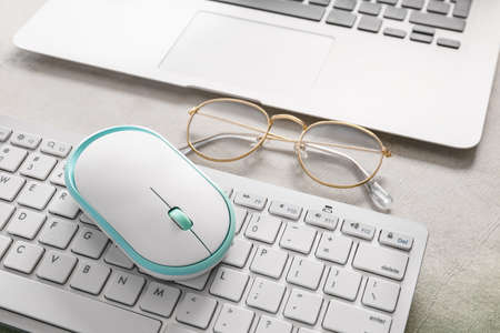 Modern PC mouse, keyboard and glasses on tableの写真素材