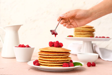 Woman pouring sweet jam onto tasty pancakes with berries on tableの写真素材