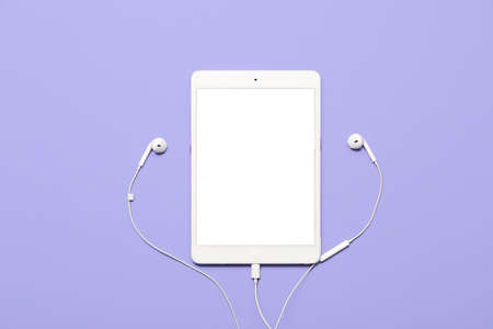 Tablet computer with earphones on color background