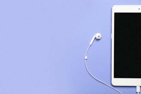 Tablet computer with earphones on color background