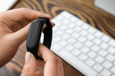Woman using fitness tracker at workplace in office, closeupの写真素材