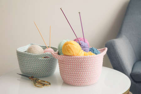 Wicker baskets with knitting yarn on table in roomの写真素材