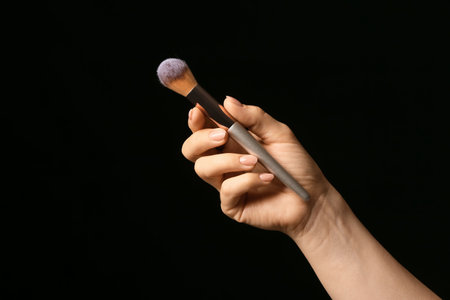 Hand with beautiful manicure holding makeup brush on dark backgroundの写真素材