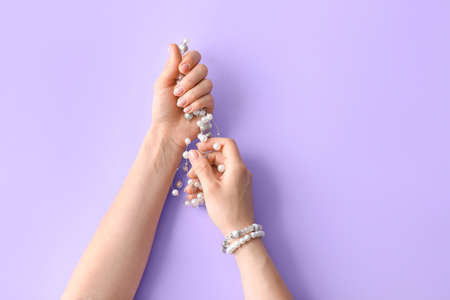 Hands with beautiful manicure holding necklace on color background