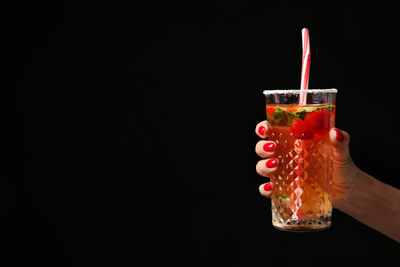 Hand with beautiful manicure holding cocktail on dark backgroundの写真素材