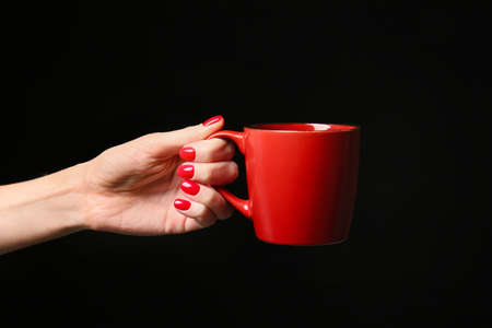 Hand with beautiful manicure holding cup on dark backgroundの写真素材