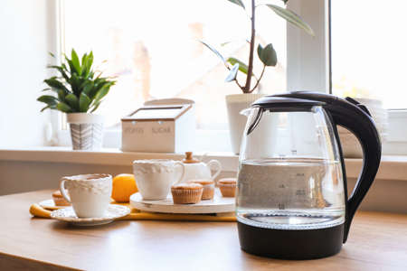 Electric kettle, cups of tea and pastry on kitchen tableの写真素材