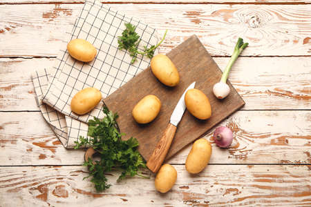 Raw potatoes with knife and cutting board on wooden tableの写真素材