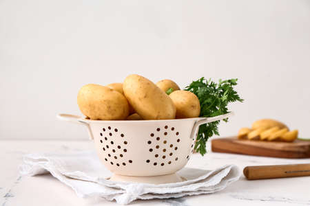 Colander with raw potatoes on light backgroundの写真素材