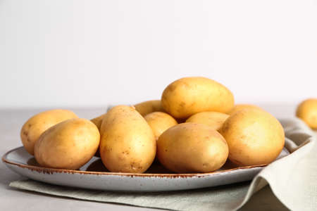 Plate with raw potatoes on light backgroundの写真素材