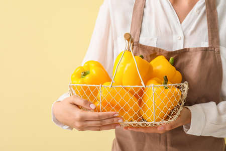 Woman with basket of yellow bell pepper on color backgroundの写真素材
