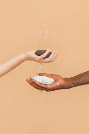 Hands of Caucasian woman and African-American man with stones on color background. Racism concept