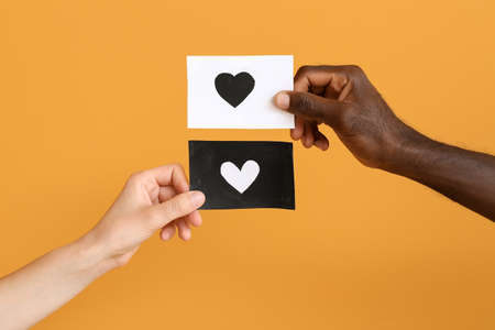 Hands of Caucasian woman and African-American man holding paper sheets with drawn heart on color background. Racism conceptの写真素材