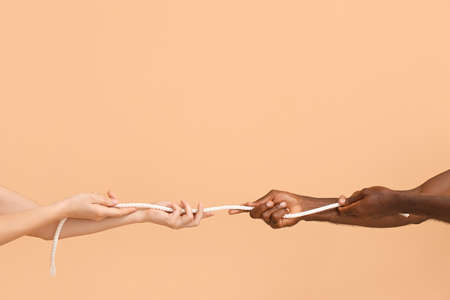 Caucasian woman and African-American man pulling rope on color background. Racism conceptの写真素材