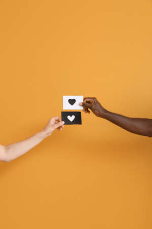 Hands of Caucasian woman and African-American man holding paper sheets with drawn heart on color background. Racism conceptの写真素材