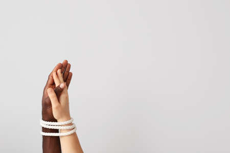 Hands of Caucasian woman and African-American man tied together with rope on light background....