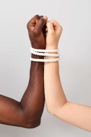 Hands of Caucasian woman and African-American man tied together with rope on light background....