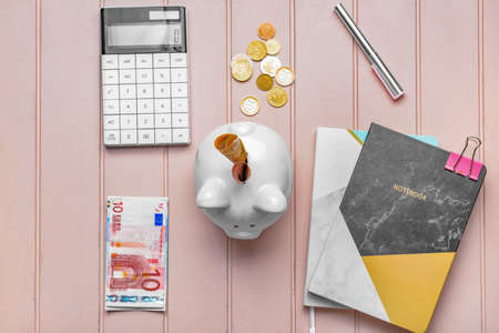 Piggy bank with money, calculator and stationery on color wooden backgroundの写真素材