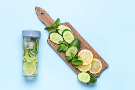 Bottle of infused water with lemon and cucumber on color background