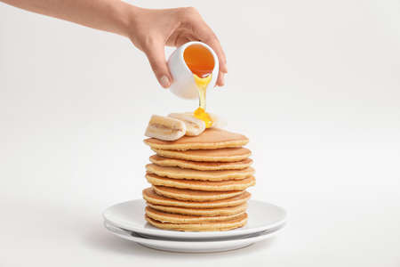 Woman pouring honey onto tasty banana pancakes on plate against white backgroundの写真素材