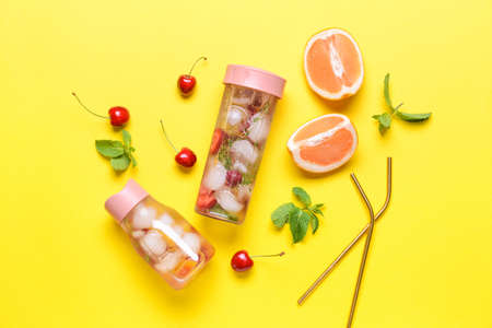 Bottles of infused water with citruses and berries on color background