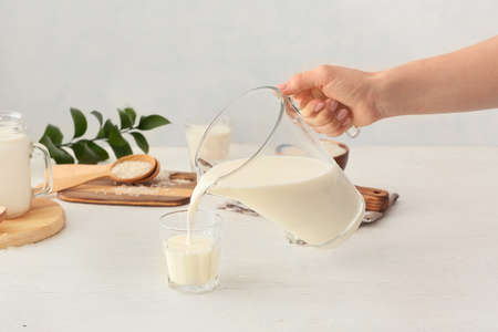 Woman pouring rice milk from jug into glass on table