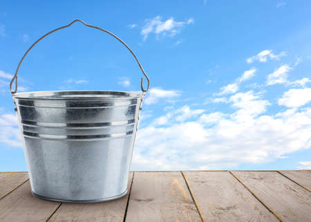 Metal bucket on wooden table outdoorsの写真素材