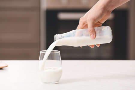 Woman pouring rice milk from bottle into glass on table