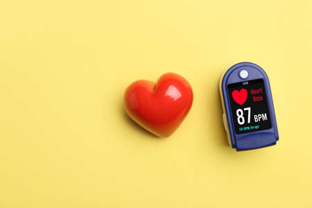 Red heart and pulse oximeter on color background