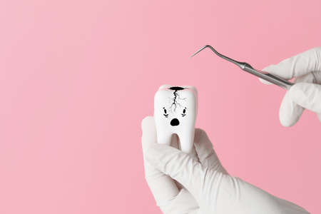 Hands of dentist with funny tooth and tool on color backgroundの写真素材