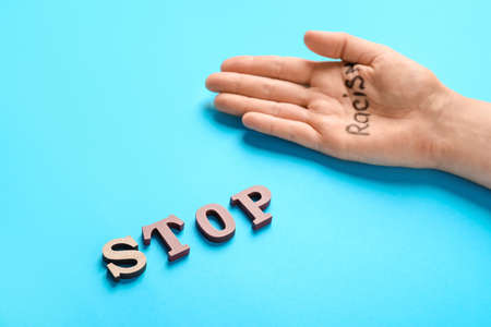 Female hand with text STOP RACISM on color background