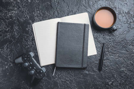 Notebooks with joypad and cup of coffee on dark background