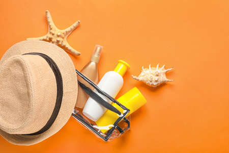 Bag with sunscreen cream and hat on color background