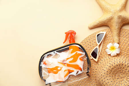 Bag with sunscreen cream, hat and sunglasses on color background