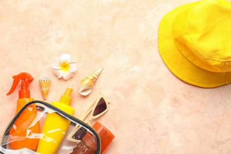 Bag with sunscreen cream, hat and sunglasses on color background