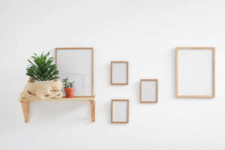 Shelf with houseplant and blank picture frames on light wall