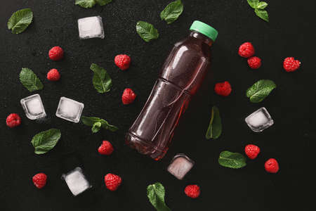 Bottle of fresh tea, mint, ice cubes and raspberry on dark background
