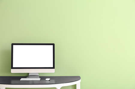 Modern computer on table near color wall