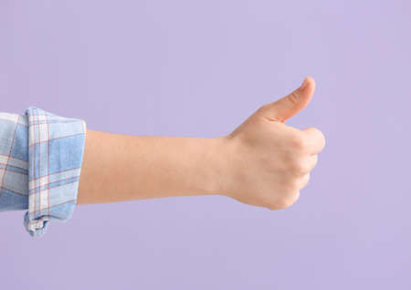 Hand of woman showing thumb-up gesture on color background