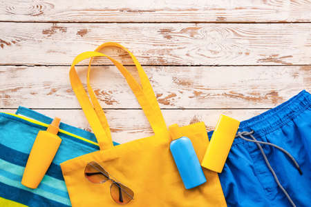 Beach bag with sunscreen cream and accessories on white wooden background