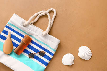 Beach bag with sunscreen cream and sunglasses on color background