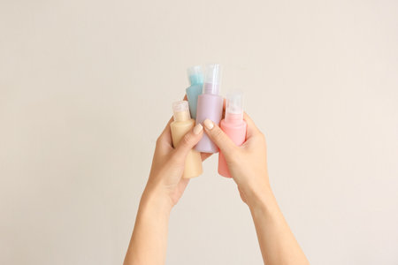 Female hands and travel bottles with body care cosmetics on light backgroundの写真素材