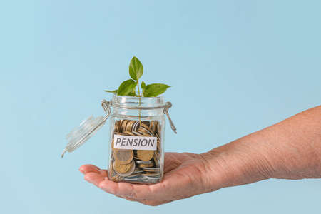 Hand of senior woman with savings and young plant in jar on color background. Concept of pensionの写真素材