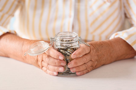 Senior woman with savings in jar at table. Concept of pensionの写真素材